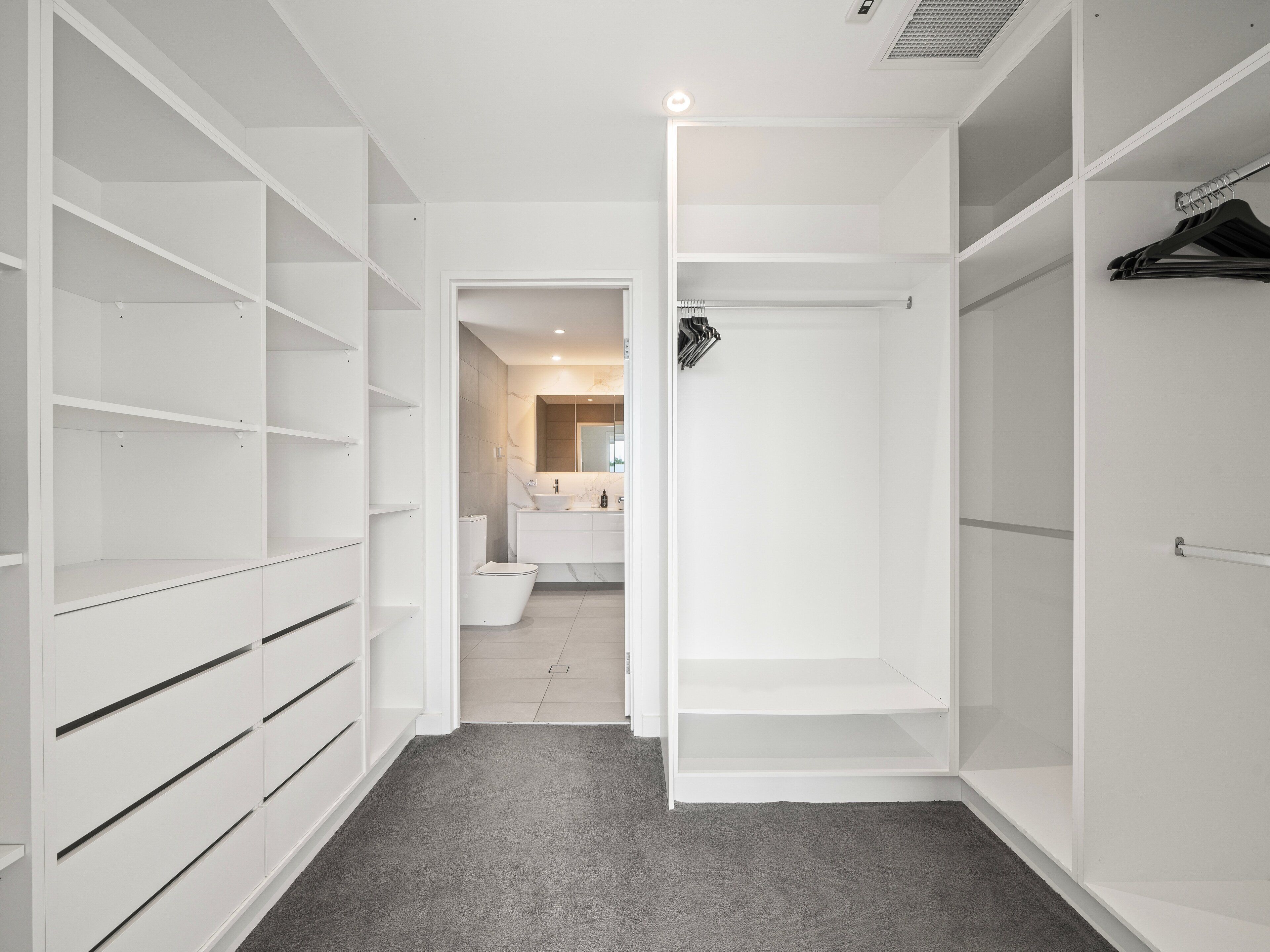 A modern, white closet with open doors revealing a bathroom with a toilet and sink.