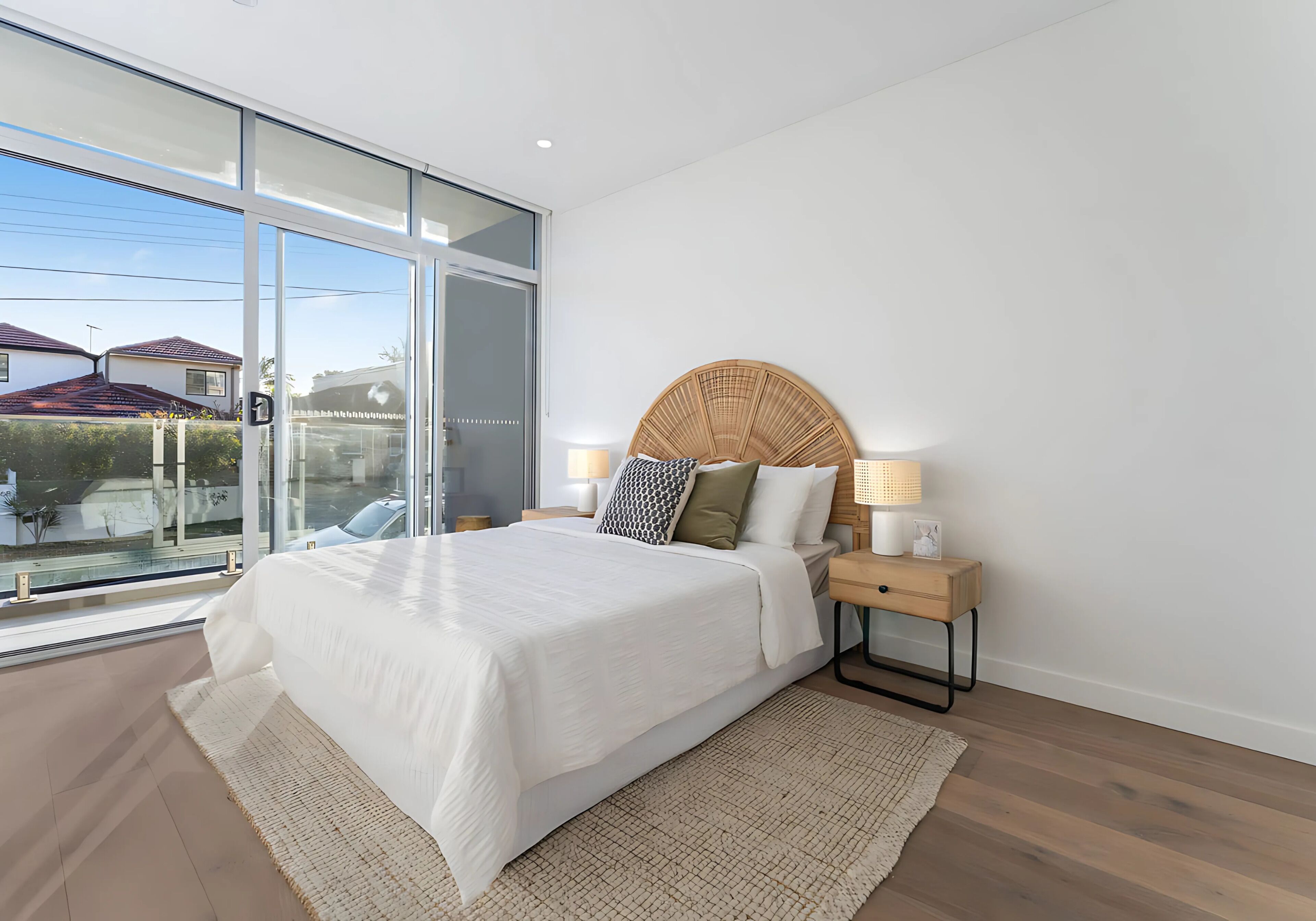 Een moderne slaapkamer met een groot bed, een nachtkastje met een lamp en uitzicht naar buiten door een schuifglazen deur.