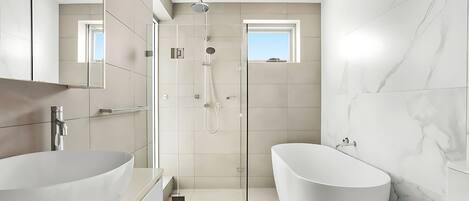 Een moderne badkamer met een vrijstaand bad, een douche met glazen wanden en een grote spiegel.