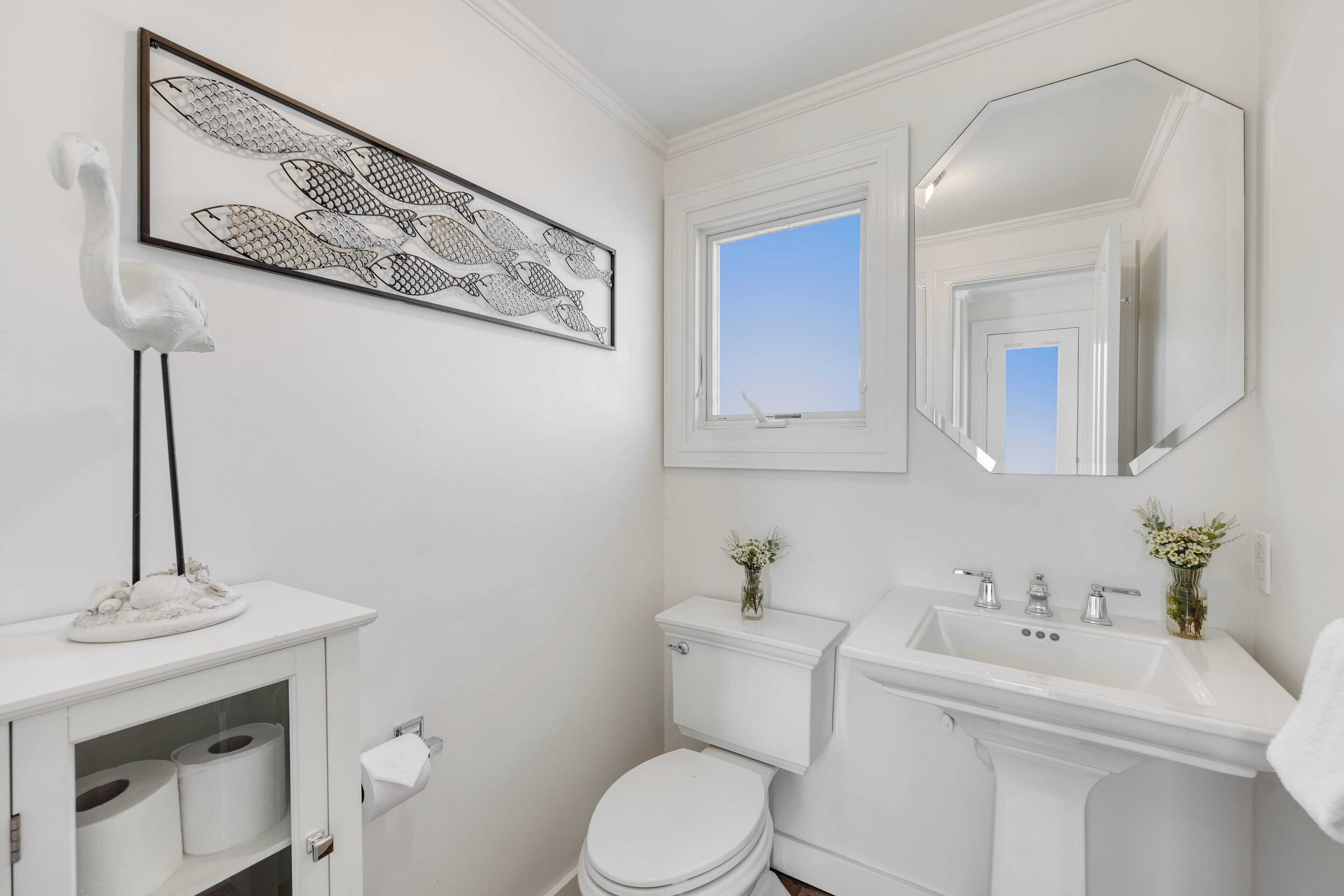 A bathroom with a toilet, sink, and a framed fish artwork.