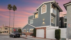 A two-story house with a garage, a stop sign, and palm trees in the background.