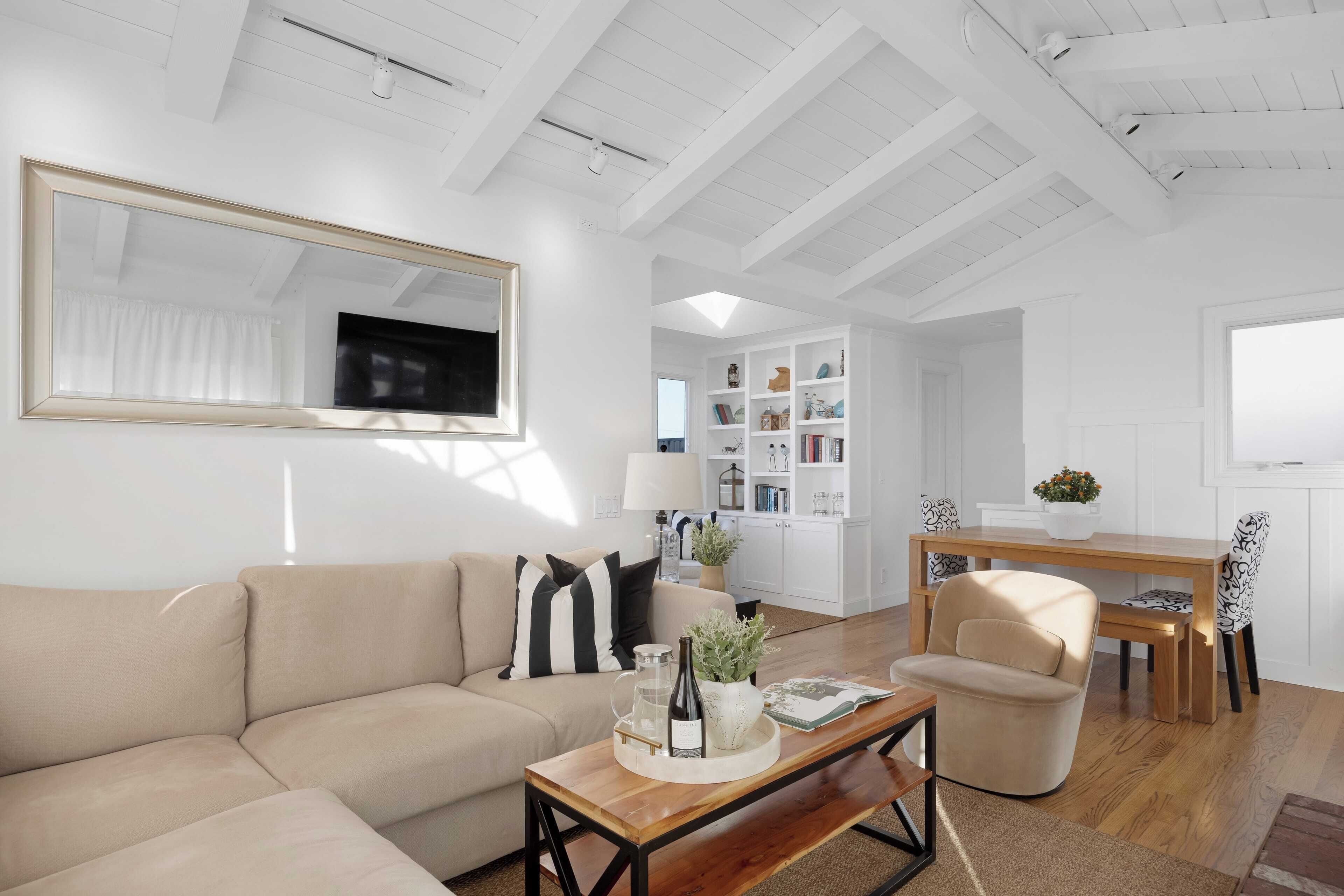 A modern living room with a beige sofa, a wooden coffee table, and a dining area with a wooden table and chairs.