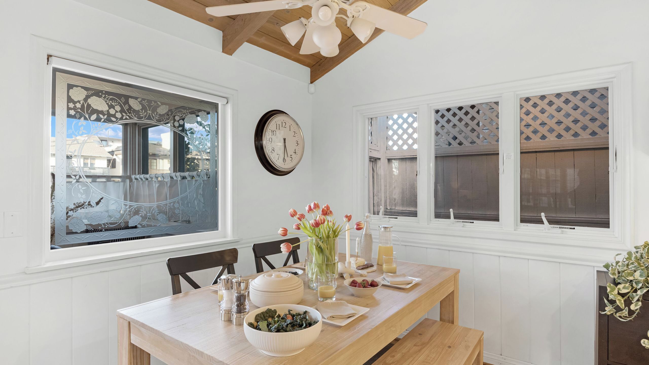Un comedor con una mesa de madera, sillas, un reloj y ventanas decorativas.