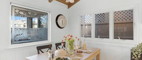 Un comedor con una mesa de madera, sillas, un reloj y ventanas decorativas.