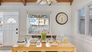 A dining area with a wooden table, a clock, a window with a decorative frame, and a door.