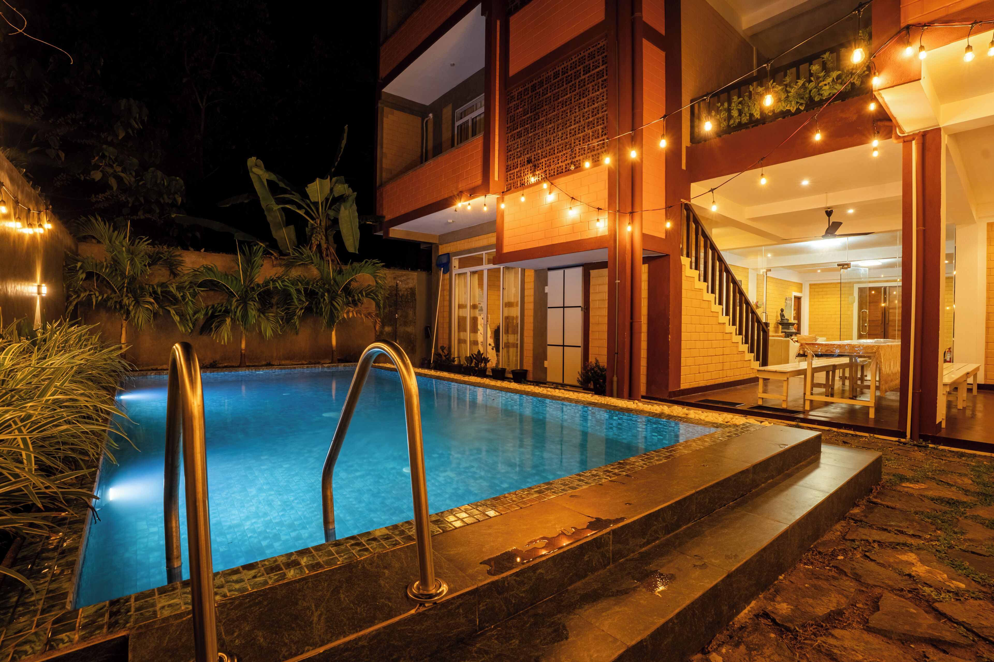 A swimming pool with steps leading into it, surrounded by plants and a building with a balcony.