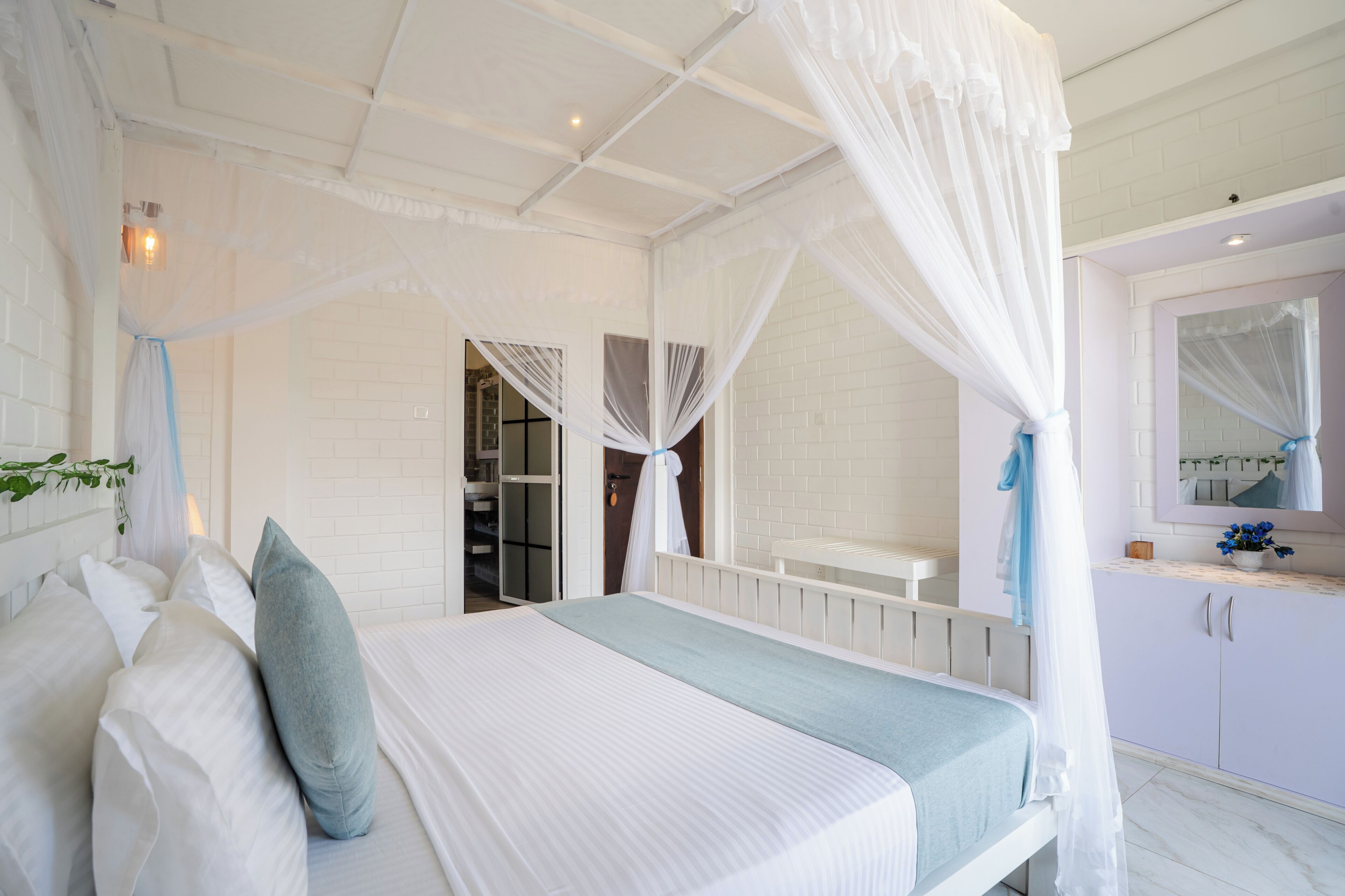 Un dormitorio con cama con dosel, vestidor y baño con espejo.