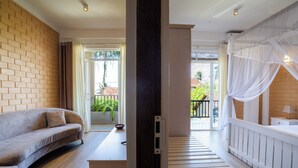 Une chambre d’hôtel avec un canapé, un lit à baldaquin, une petite table et une vue sur l’extérieur.