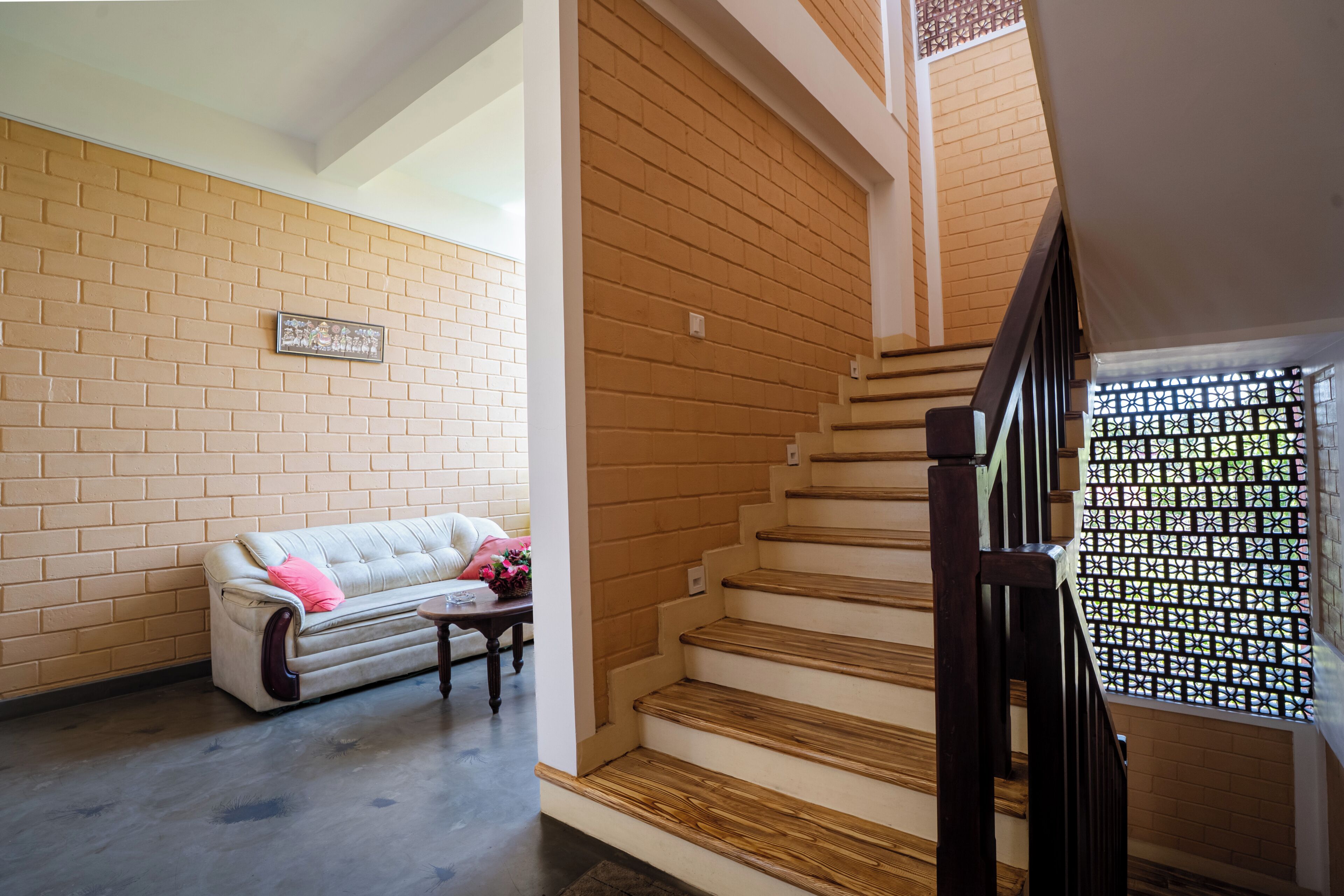 A staircase with wooden steps and a black railing, leading to a room with a brick wall and a white sofa with a pink pillow.