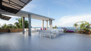 Une terrasse extérieure avec des bancs et des tables blancs, une vue sur la mer et un ciel dégagé.