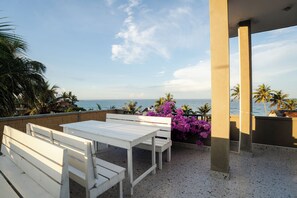 Una terraza con mobiliario blanco, vista al mar y palmeras.