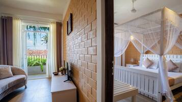 A room with a brick wall, a bed with a canopy, a sofa, a small table, and a view of the outdoors.