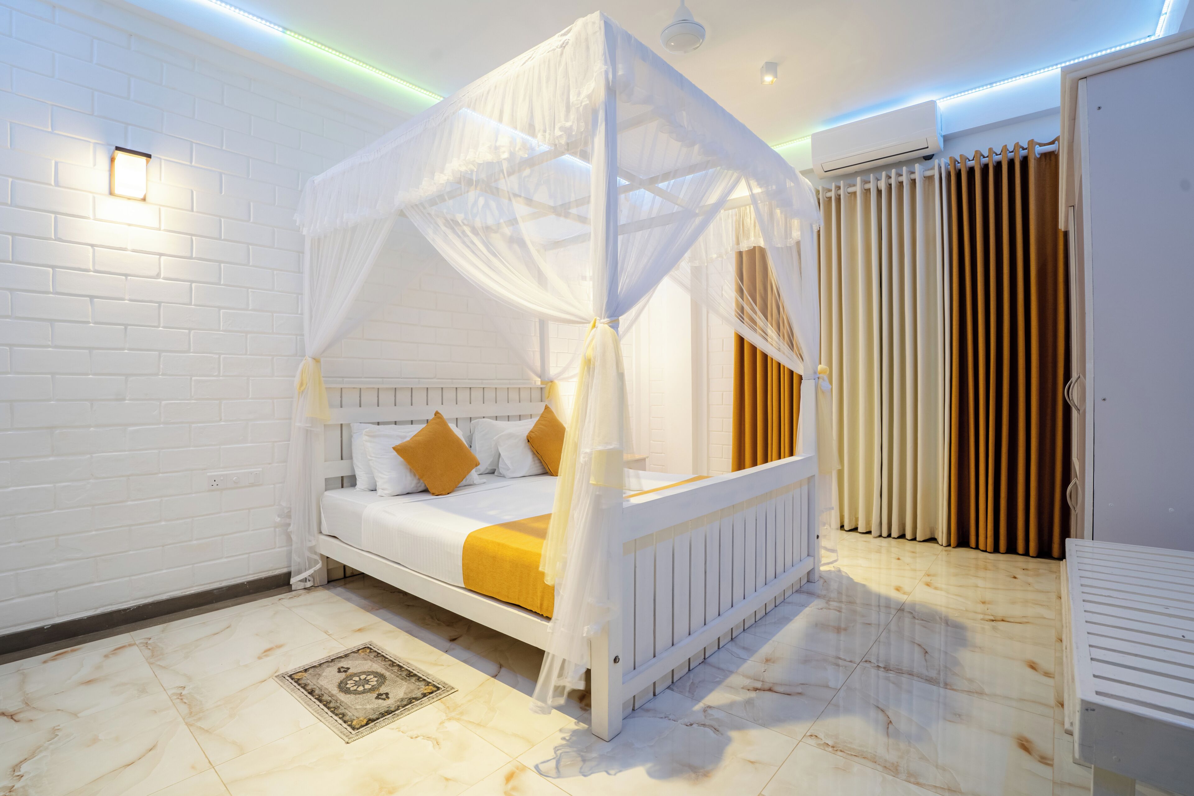 Une chambre avec un lit sous un dais, un mur en briques blanches, un radiateur et une porte avec des rideaux.