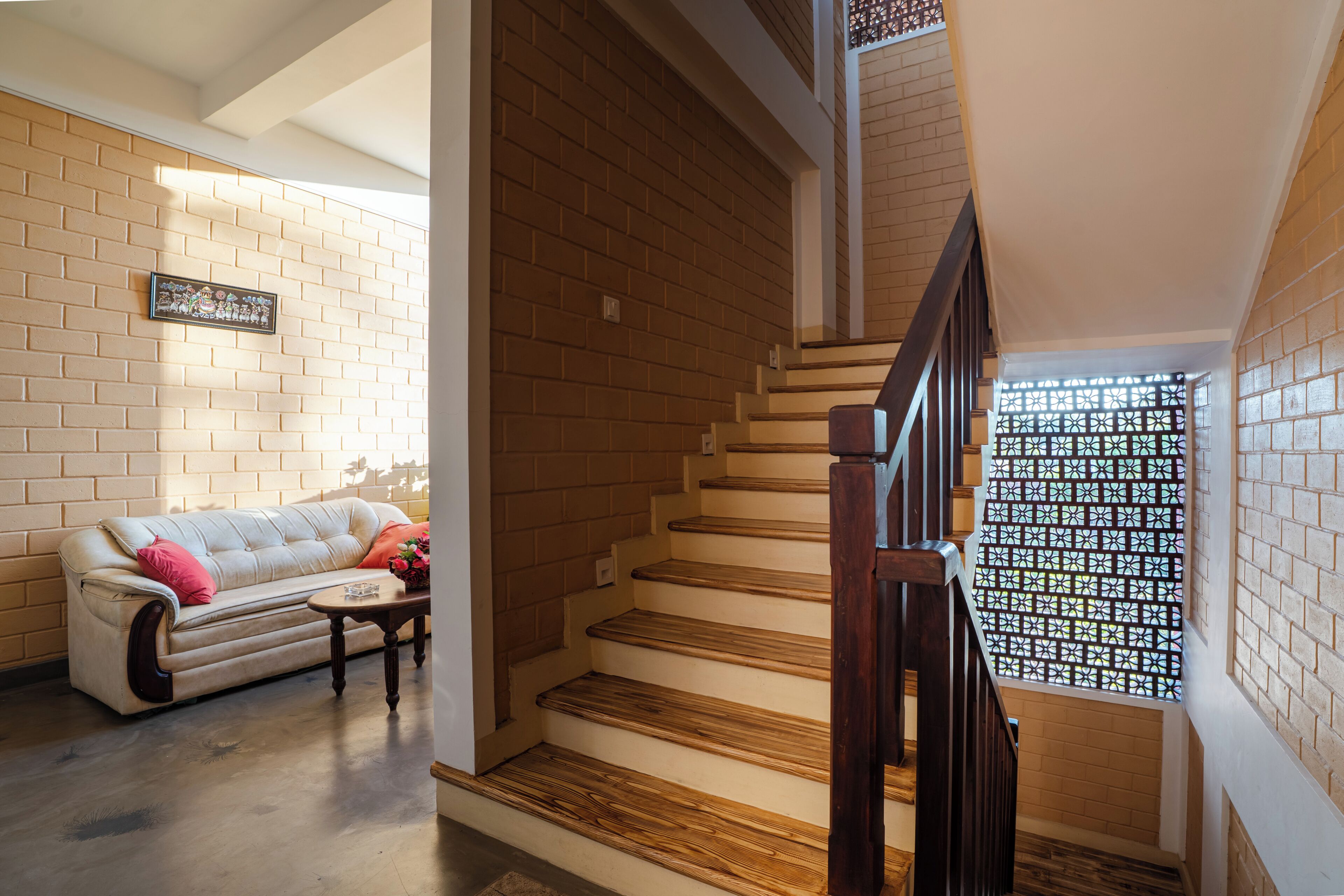 A staircase with wooden steps and a dark handrail, leading to a room with a brick wall and a white ceiling.