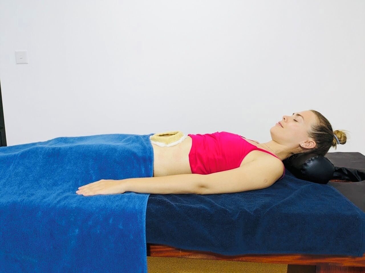 A person lying on a massage table with a blue sheet, wearing a red top and yellow shorts.