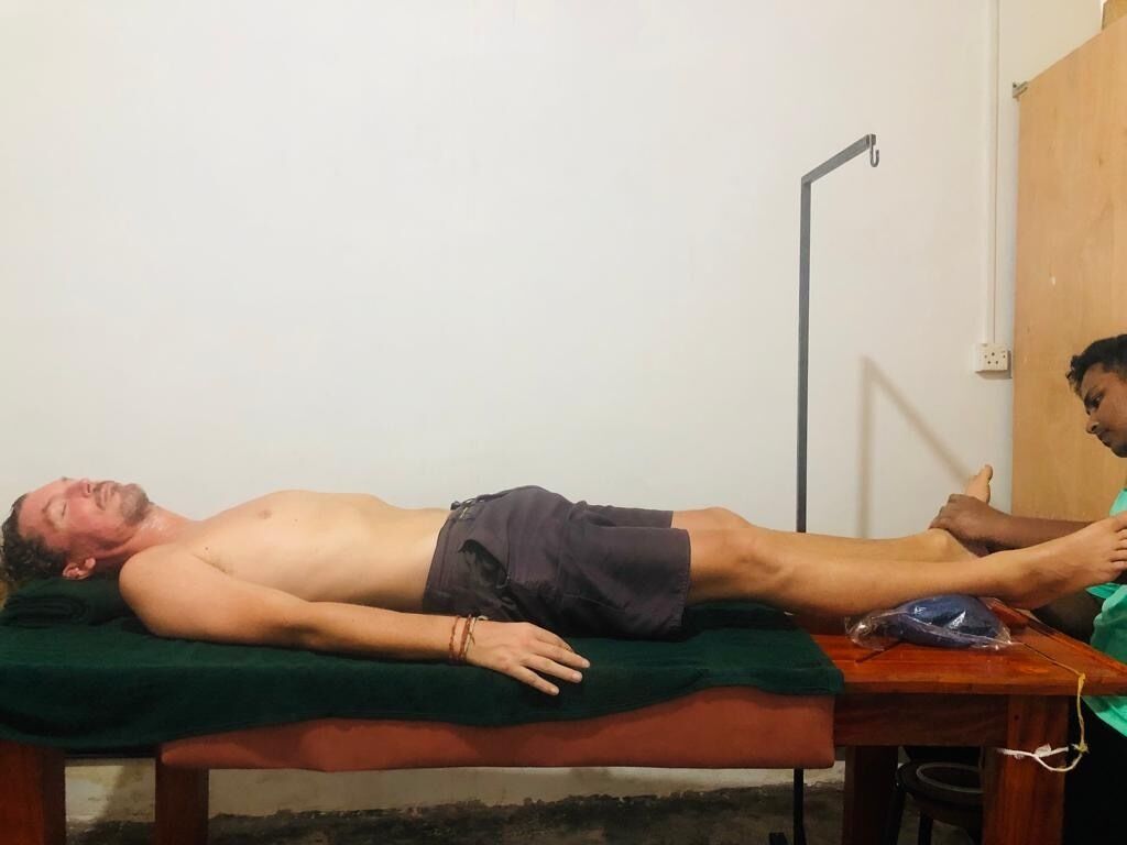 Une personne allongée sur un tapis vert, sur une table en bois, dans une pièce dont le mur est blanc et la porte est en bois.