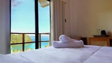 Habitación de hotel con una cama grande, vistas a un paisaje tropical y una mesita de noche de madera con una lámpara.