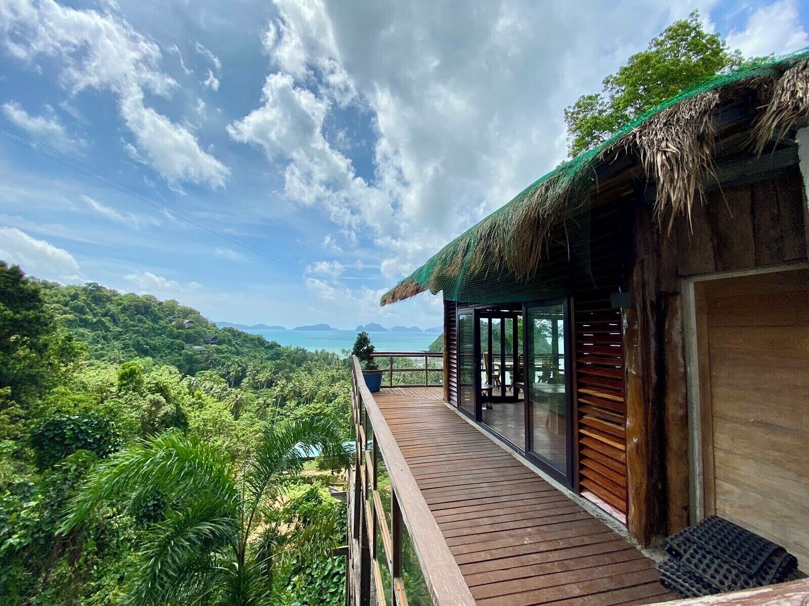 Una terraza de madera con cerramiento de vidrio que da a un paisaje verde exuberante y una vista distante del océano.