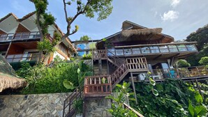 A multi-level wooden structure with a thatched roof, surrounded by lush greenery and stone walls. - 89 Villas Resort and Spa by Hiverooms (El Nido)