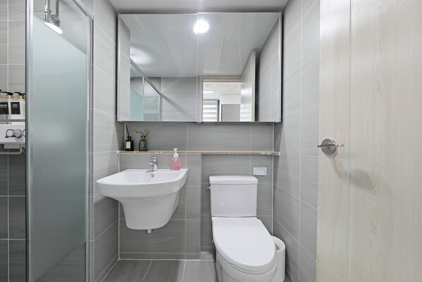 Un baño moderno con cabina de ducha de vidrio, un lavamanos blanco y un inodoro.