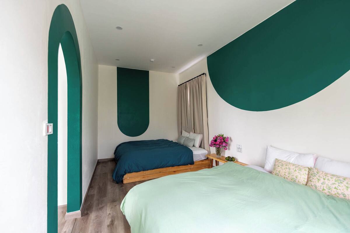 A bedroom with two beds, a wooden headboard, a nightstand, and a wall-mounted shelf with a vase of flowers.