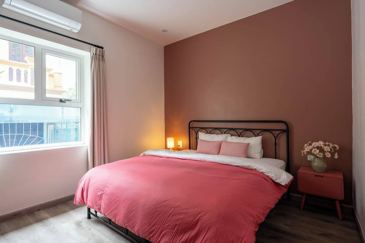 A bedroom with a bed, a nightstand, a window, and a wall-mounted air conditioner.