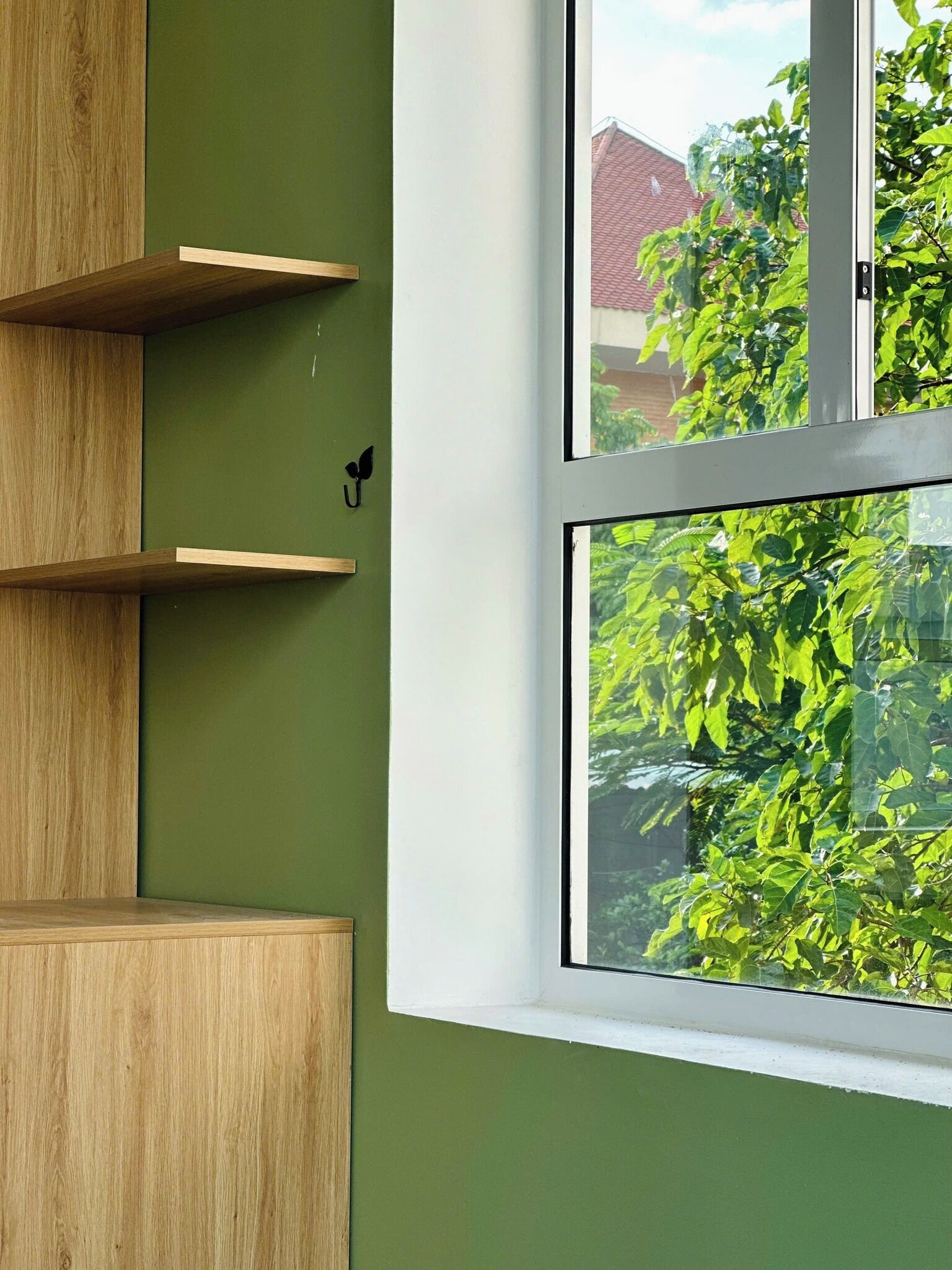 Une pièce avec un mur vert, une fenêtre donnant sur des arbres et des étagères en bois.