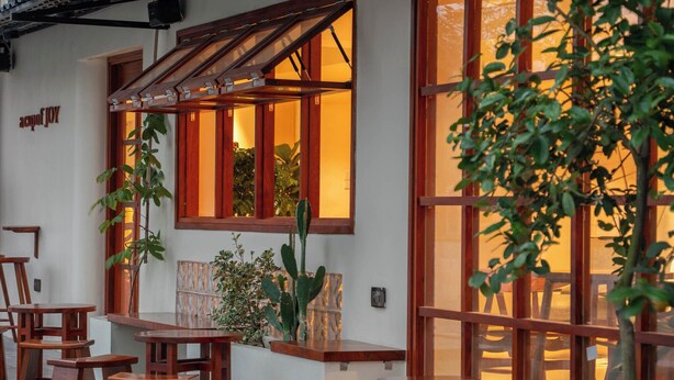 Un bâtiment doté de grandes fenêtres, de tabourets en bois et de plantes en pot.
