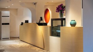 Un espace d’accueil au design moderne, comprenant un comptoir d’accueil incurvé, un grand vase rempli de fleurs et un élément décoratif mural.
