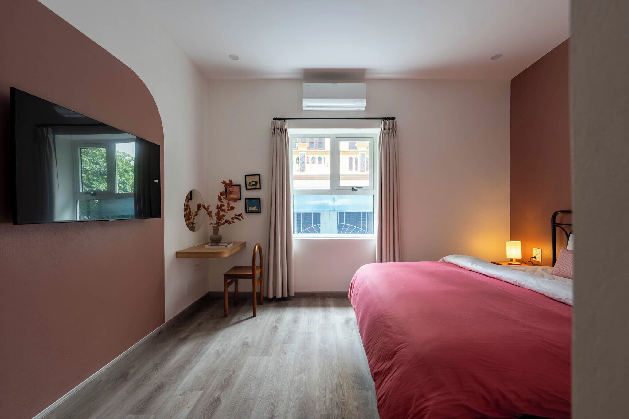 A bedroom with a bed, a desk, a chair, a TV mounted on the wall, and a window with curtains.