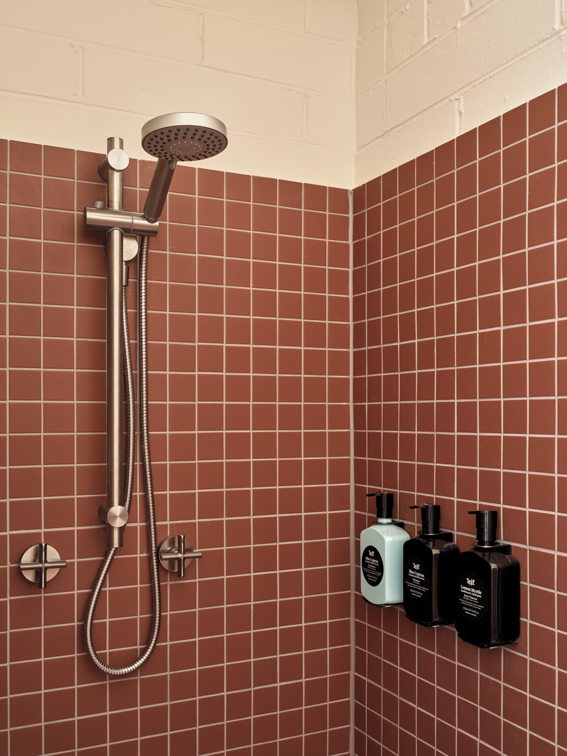 A shower with a handheld showerhead and a wall-mounted control panel.