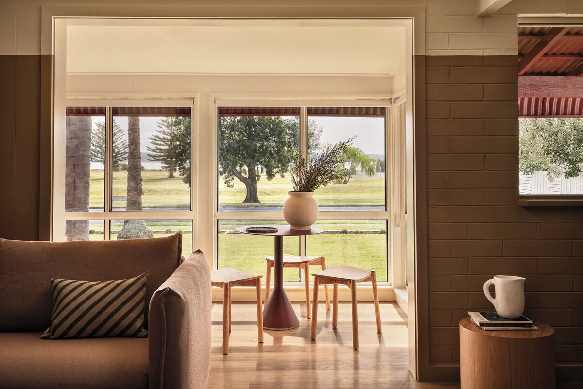 A cozy living room with a sofa, a coffee table, and a view of a grassy area through large windows.