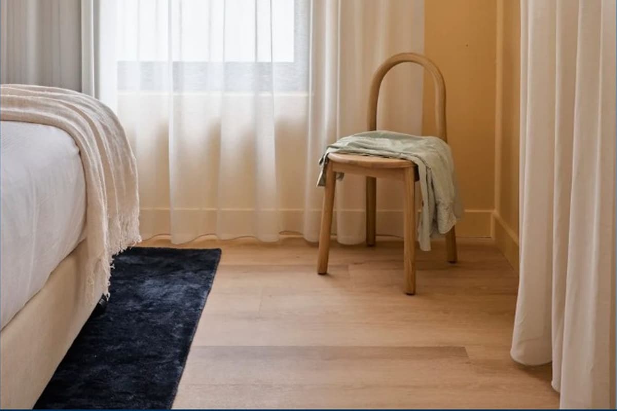 A bedroom with a bed, a chair, a window with curtains, and an air conditioning unit.