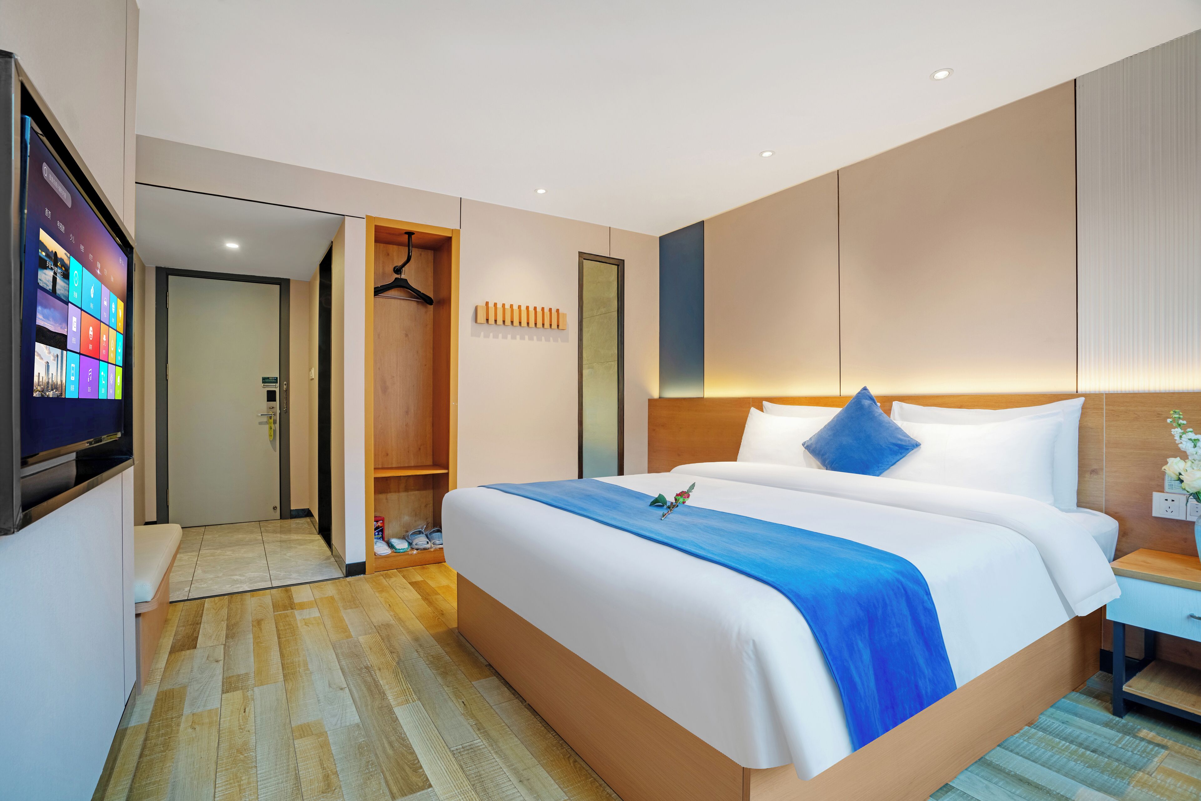 Habitación de hotel con una cama grande, un armario de madera, un televisor y un baño visible a través de una puerta abierta.