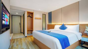 Habitación de hotel con una cama grande, un armario de madera, un televisor y un baño visible a través de una puerta abierta.