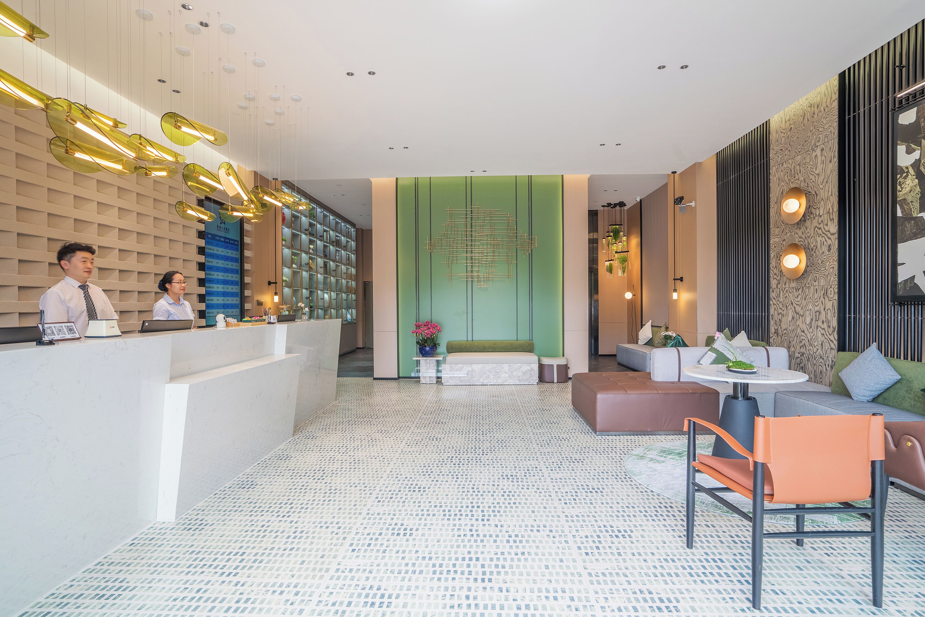 A modern hotel lobby with a reception desk, seating area, and decorative lighting.