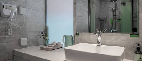 A bathroom with a white sink, a handheld hair dryer, a green kettle, and a shower with a glass door.