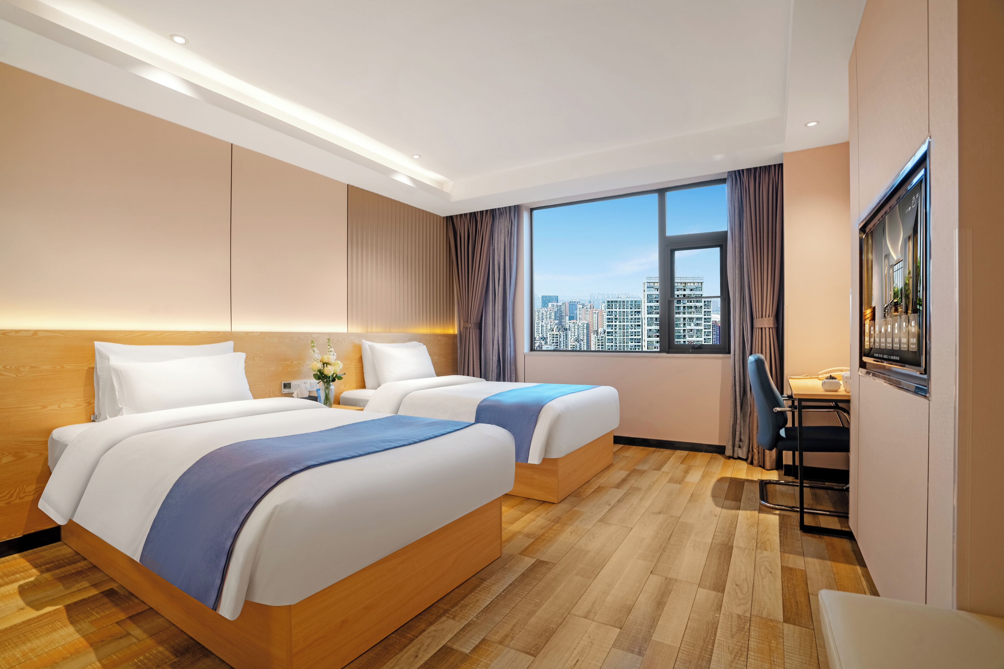 Habitación de hotel con dos camas, un escritorio, una silla, un televisor y vista a la ciudad.