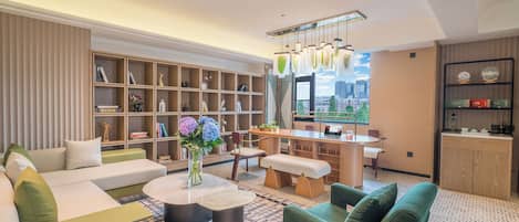 A modern living room with a sofa, a coffee table, a bookshelf, and a view of the city.