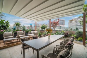 A rooftop terrace with outdoor seating, a table, and a vase of flowers.