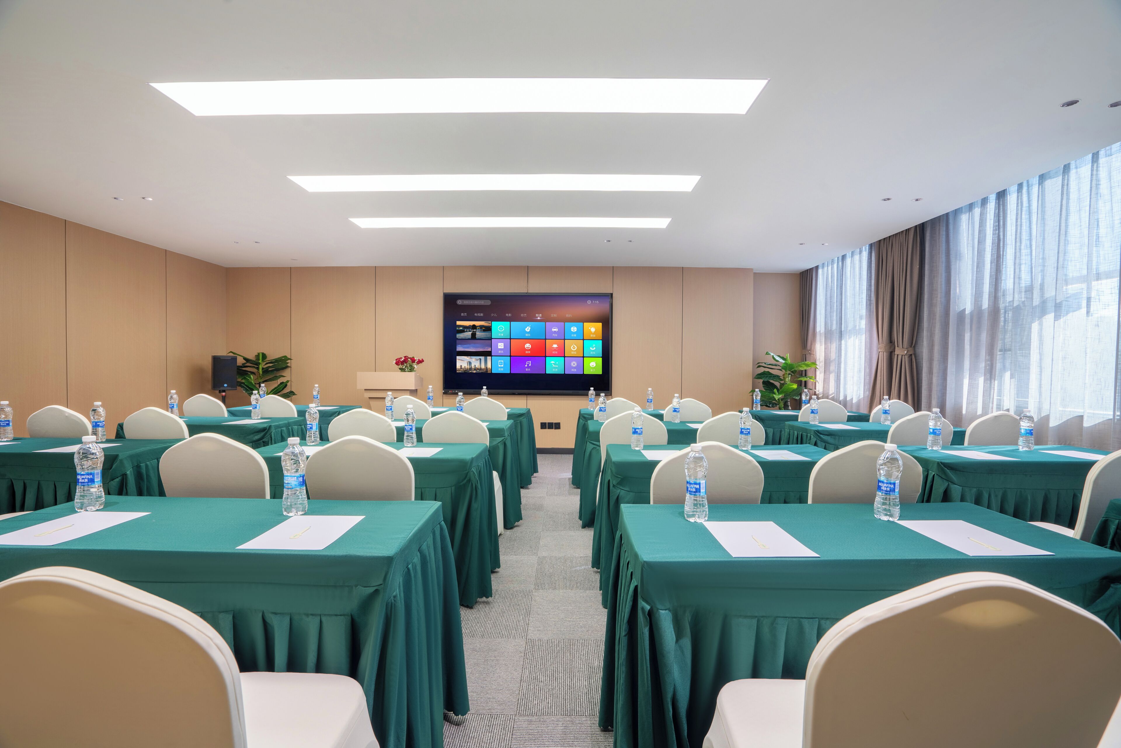 A conference room with tables, chairs, a projector screen, and a large window.