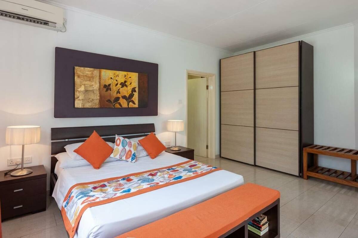 A modern hotel room with a large bed, two bedside tables with lamps, a wardrobe, and a bench with books.