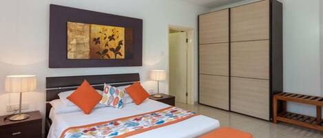 A modern hotel room with a large bed, two bedside tables with lamps, a wardrobe, and a bench with books.