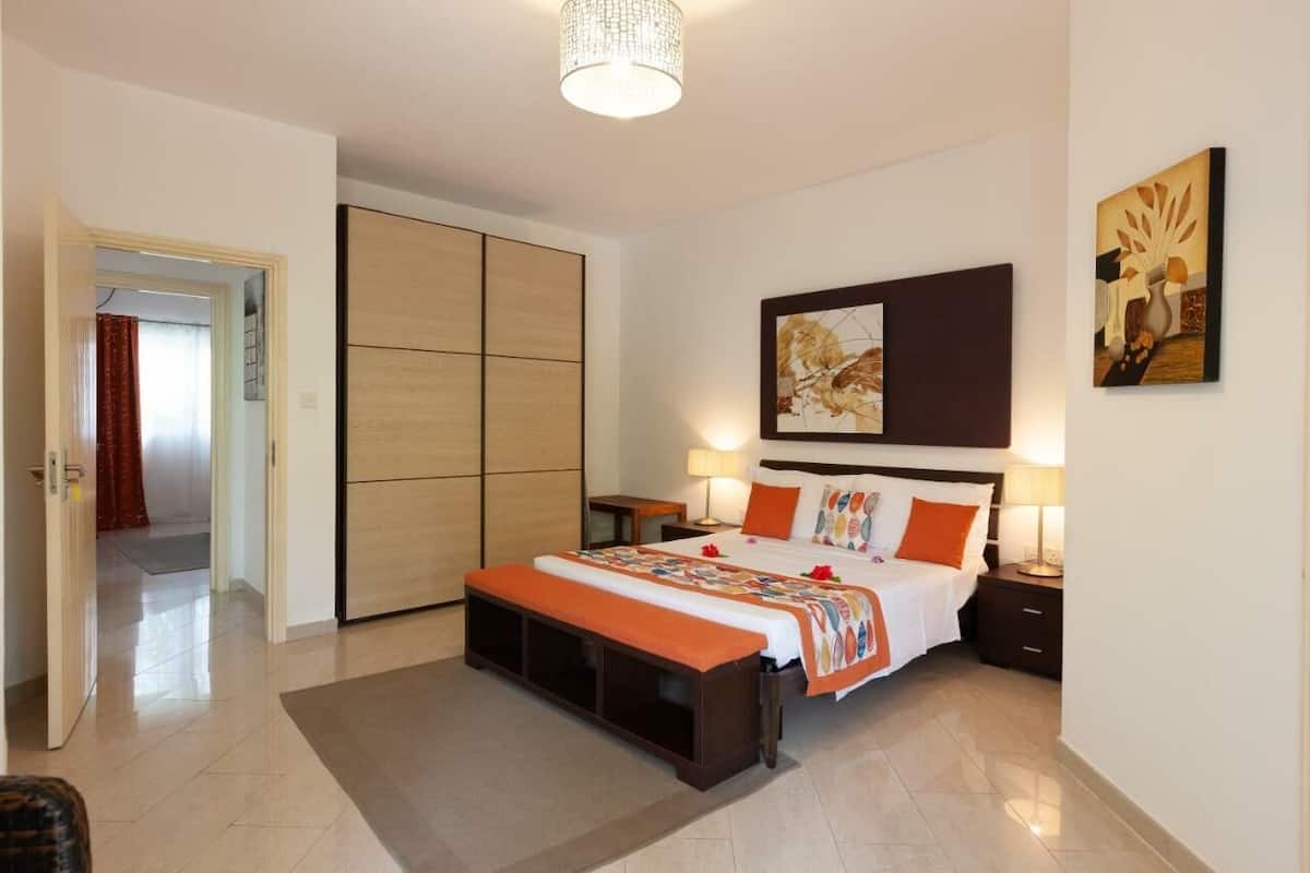 A modern hotel room with a large bed, a wardrobe, a bench, and artwork on the walls.