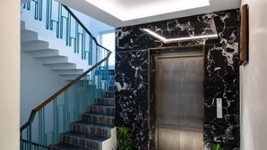 Et moderne interiør med et geometrisk gulvmønster, en trappe med blå gelændere og en marmorvæg med elevator.