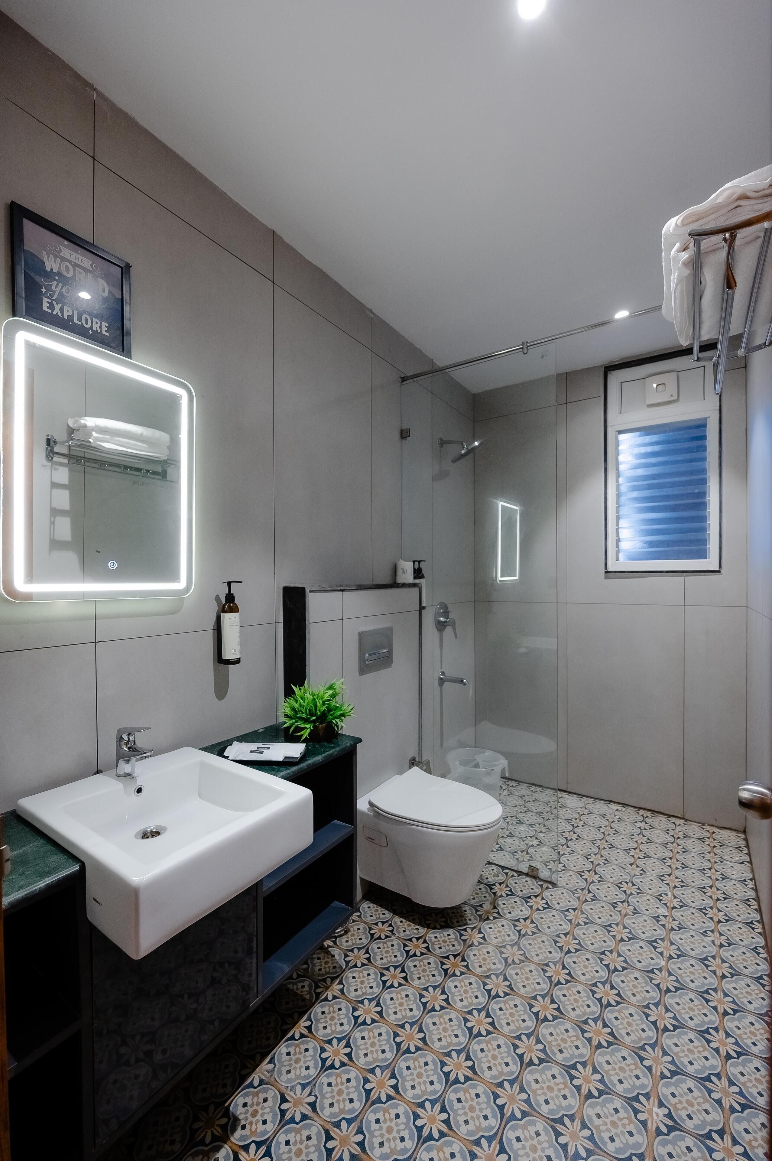 A modern bathroom with a large mirror, a sink, a toilet, and a shower.