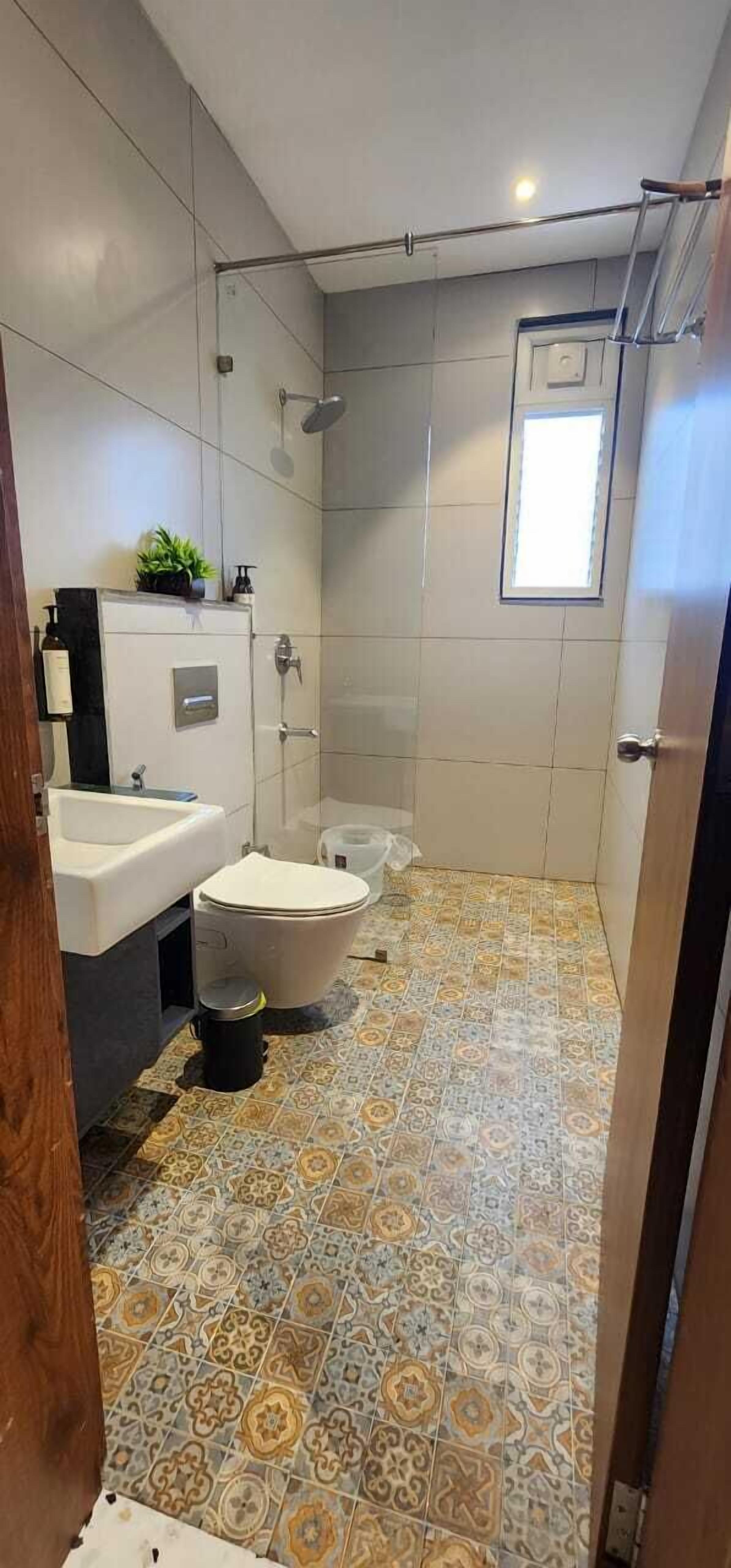 A bathroom with a toilet, bidet, and shower. It has patterned floor tiles and a small window.