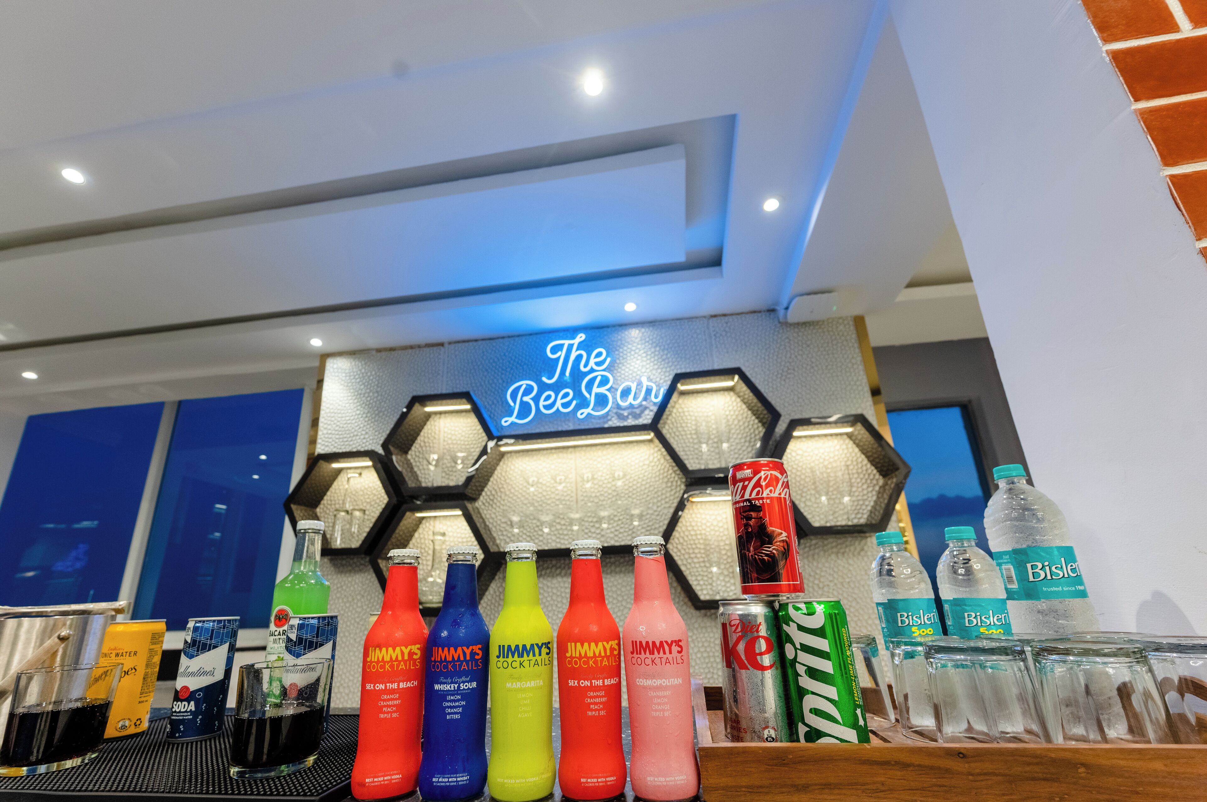 A bar area with a neon sign reading "The Bee Bar" and various bottles of beverages.