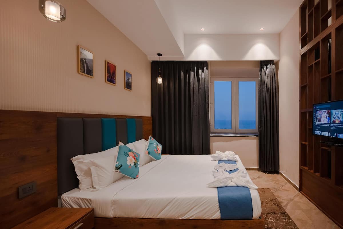 A hotel room with a large bed, a television, a window with curtains, and a wooden headboard.