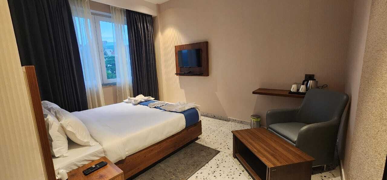 A hotel room with a bed, a TV mounted on the wall, a chair, and a small table.